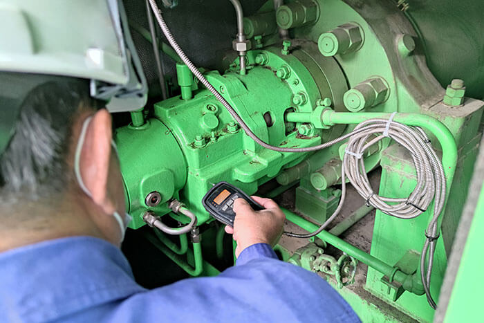 Person mit Schutzkleidung führt mittels eines kleinen Messgeräts eine Schwingungsmessung an einem Elektromotor durch