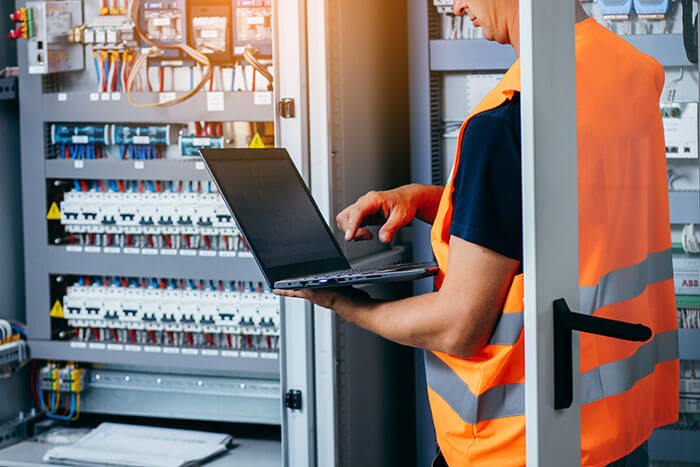 Person in high-visibility vest and with laptop in front of a control cabinet
