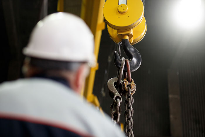 leistungen-anschaffung-von-kranen Eine Person schaut herauf zu einem Kranhaken in einer Industrieanlage